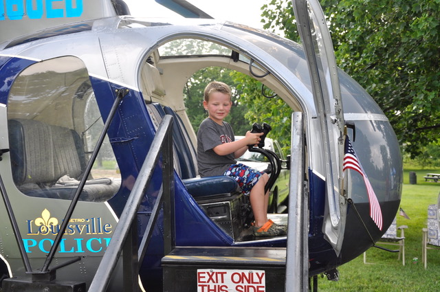 Boy sitting in a Louisville Police helicopter cockpit, smiling at controls.